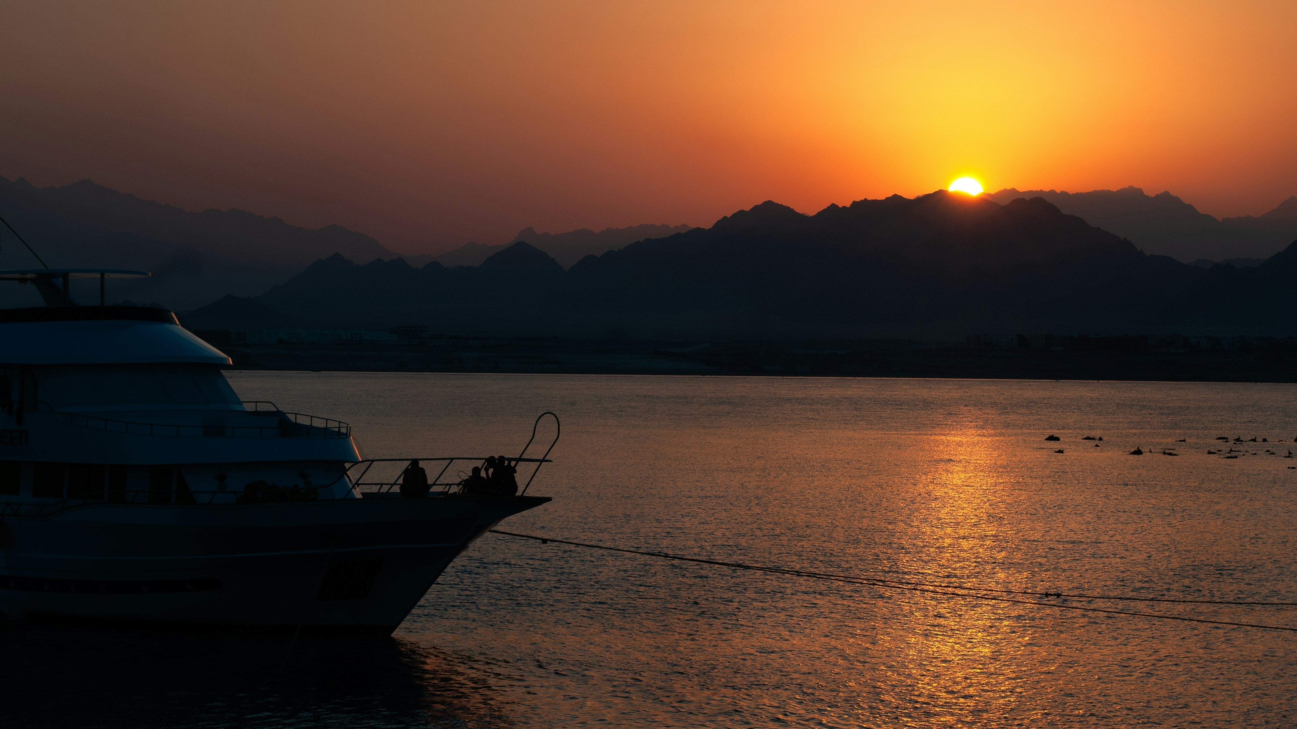 A boat anchored on the water during a vibrant golden hour sunset behind distant mountains.