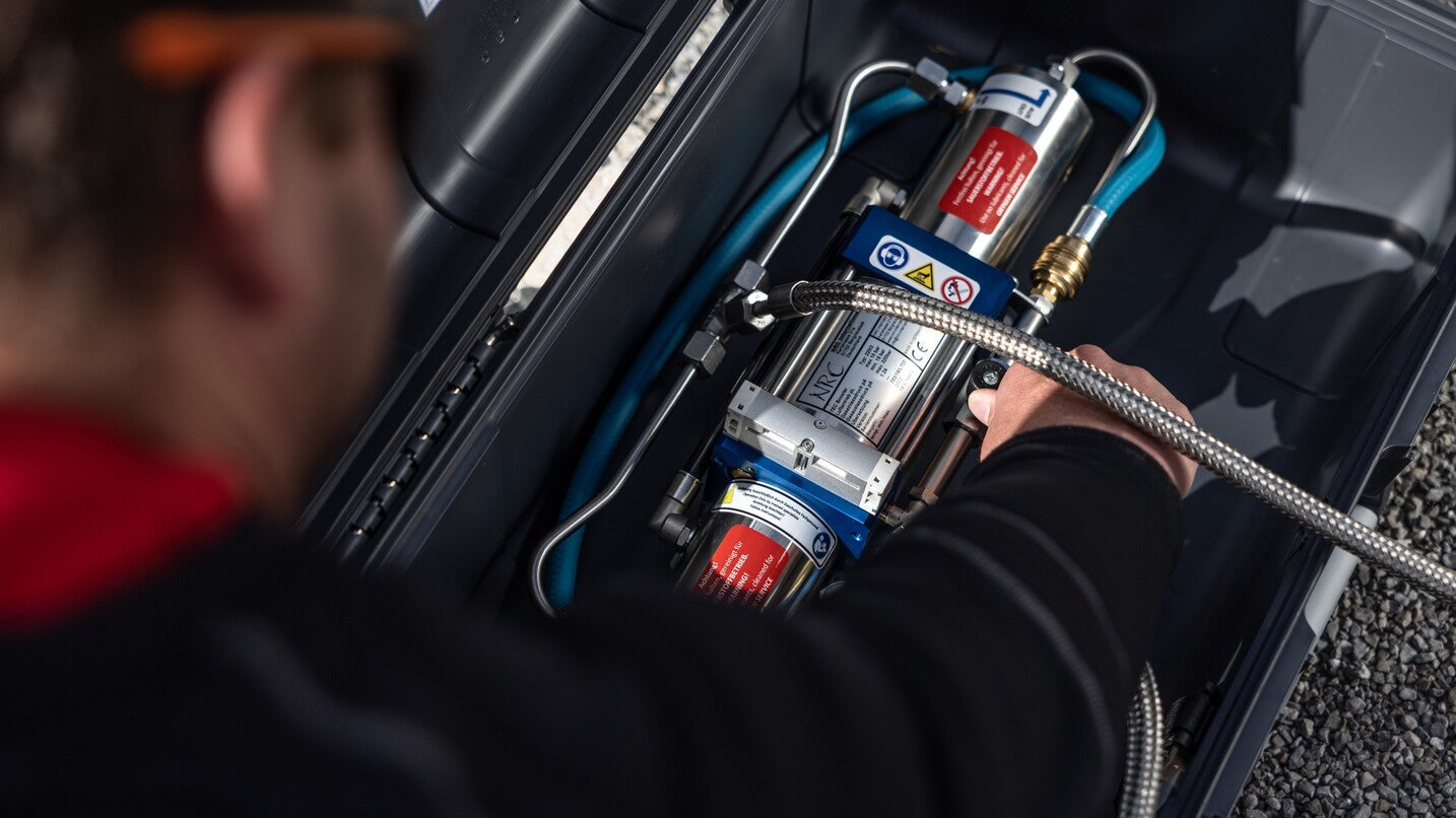 Technician operating an NRC oxygen booster inside a protective case, showing high-pressure lines and fittings used for safe oxygen compression.