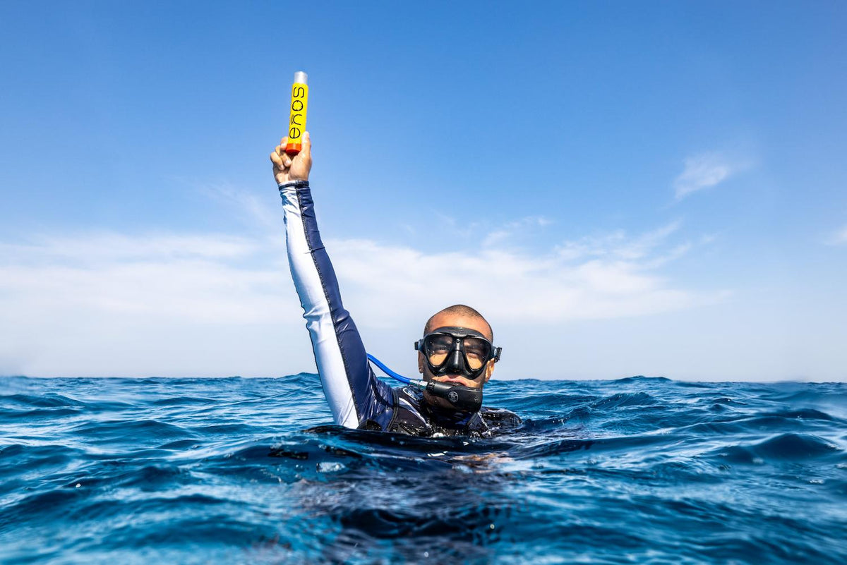 A diver floating in open water, holding a yellow rescue beacon high above the surface.