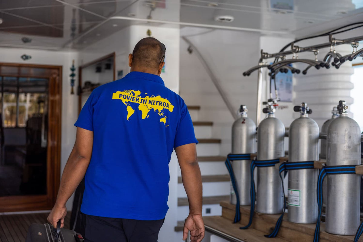 A service technician wearing a blue shirt walking past a row of scuba tanks.